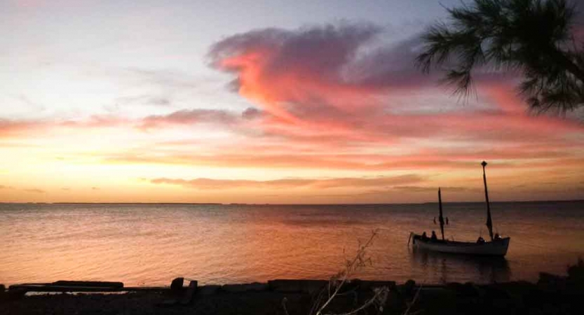 a sailboat floats in calm water at sunset